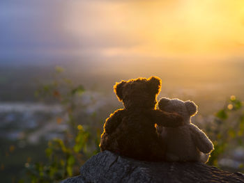 Stuffed teddy bears on rock against sky during sunset