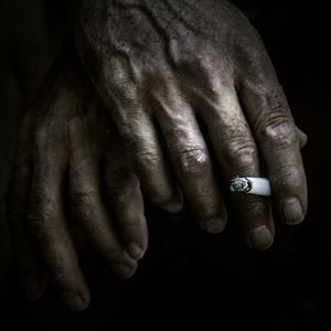 Cropped hand holding cigarette against black background
