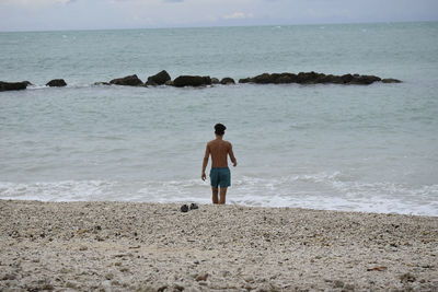 Rear view of shirtless man standing on beach