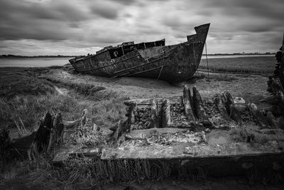 Damaged boat on land against sky