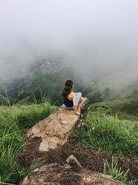 Rear view of woman on cliff over landscape during foggy weather