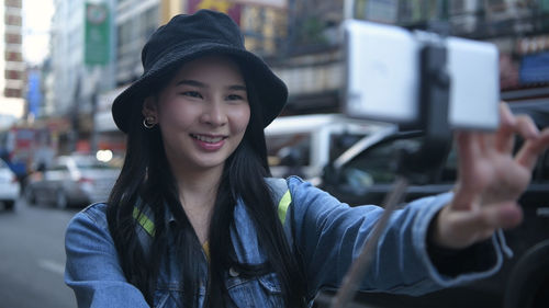 Portrait of smiling young woman using mobile phone in city