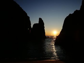 Silhouette rocks by sea against sky during sunset