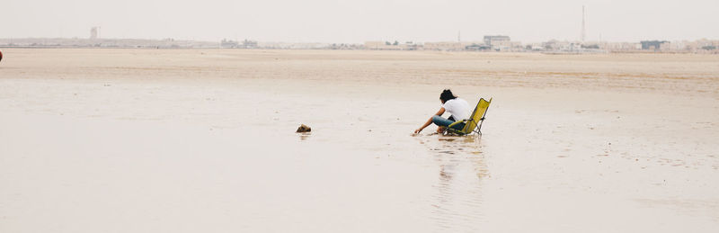 Full length of woman sitting on beach against sky