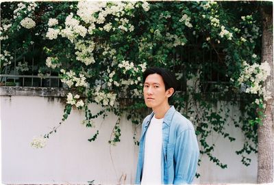 Man looking away while standing by tree against plants