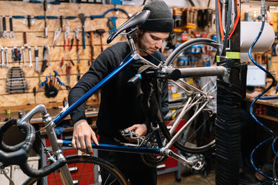 Side view of serious male mechanic repairing wheel of bicycle while working in workshop