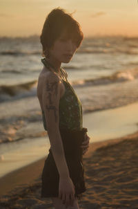 Woman standing at beach against sky during sunset