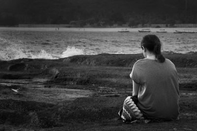 Rear view of man sitting on beach against sky