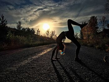 Full length of girl exercising on road during sunset