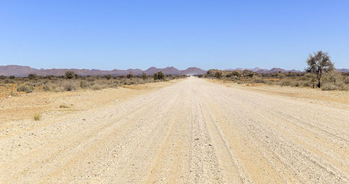 Dirt road amidst desert against clear sky