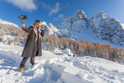 Blonde girl with a snowball in her hand take photo with phone of awesome snowy landscape, dolomites