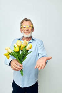 Portrait of young man holding red flowers against white background