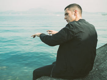 Rear view of man sitting by sea 