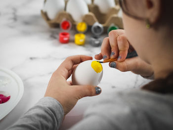 Little caucasian girl paints an easter egg with a brush with yellow acrylic pain