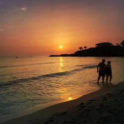 Silhouette people on beach against sky during sunset