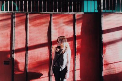 Young woman standing against red wall