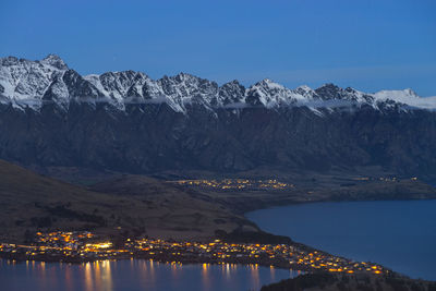 Scenic view of river by snowcapped mountains against clear blue sky at night