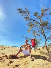 Side view of woman sitting on beach against sky