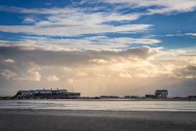 Scenic view of stilt houses and wooden seabridge at low tide north sea beach  against dramatic sky