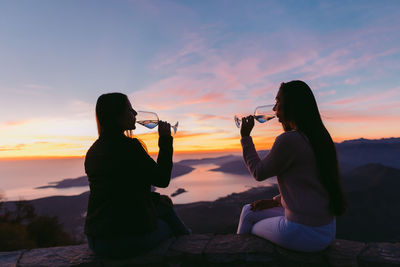 Woman photographing at beach against sky during sunset