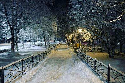 Snow covered footpath by canal in city at night