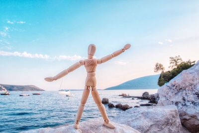 Human figurine on rocks by sea against sky