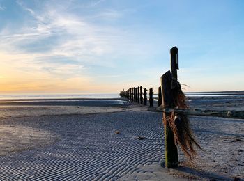 Wooden posts on beach against sky during sunset