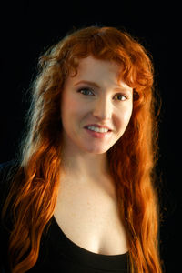 Portrait of smiling young woman against black background