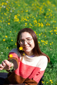Happy charming young woman is holding a little yelllow flower in front of camera. selective focus