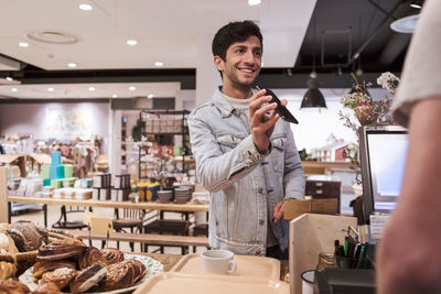 Male customer showing mobile phone while doing contactless payment to cashier at cafe