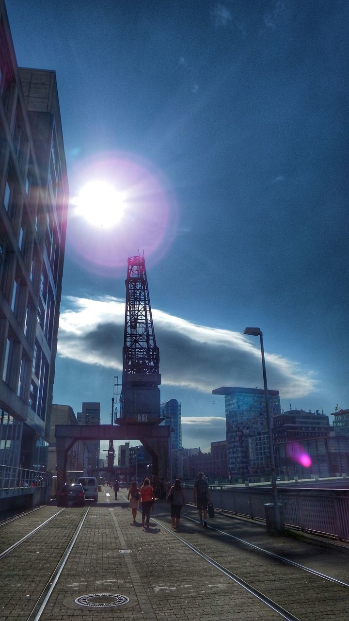 architecture, building exterior, built structure, sky, transportation, street, city, road, sun, sunlight, street light, the way forward, lens flare, car, land vehicle, sunbeam, incidental people, mode of transport, outdoors, cloud - sky