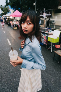 Portrait of woman having drink while standing on footpath