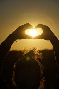 Close-up of hand holding heart shape against sky during sunset