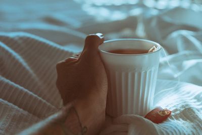 High angle view of hand holding coffee cup on bed