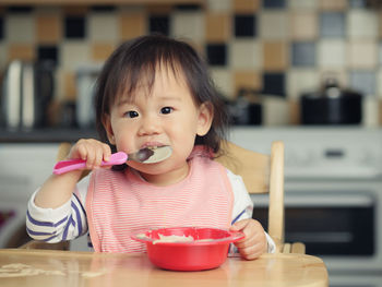 Portrait of baby girl eating food while sitting on high chair at home