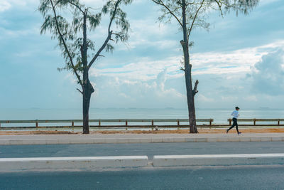 Man walking on road by sea against sky