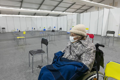 Senior women wearing protective face mask and warm clothing sitting on wheelchair at vaccination center