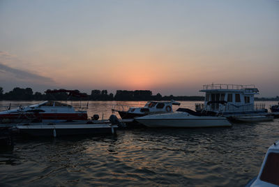 Boats moored at harbor against sky during sunset