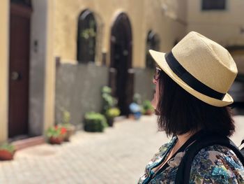 Woman wearing hat standing on footpath in city