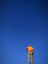 Low angle view of man standing against clear blue sky