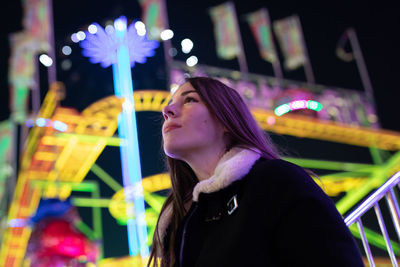 Portrait of young woman looking away while standing at night