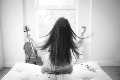 Rear view of woman sitting against curtain