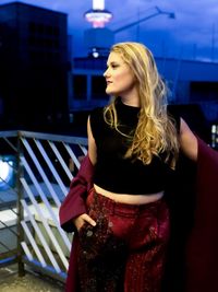 Young woman standing at building terrace in city during dusk