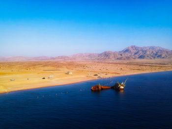 Scenic view of sea and mountains against clear blue sky