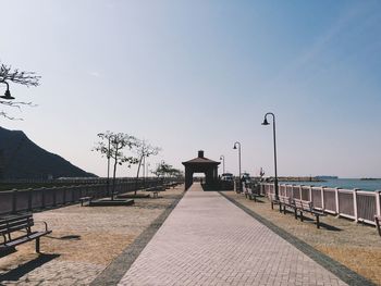 Empty walkway against clear sky on sunny day