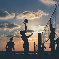 Silhouette men playing volleyball at beach against sky