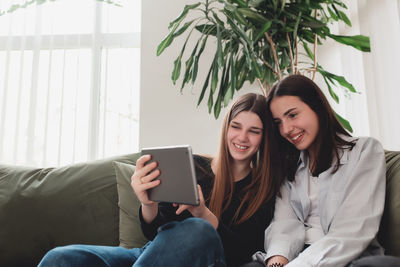 Smiling young woman using phone while sitting on sofa