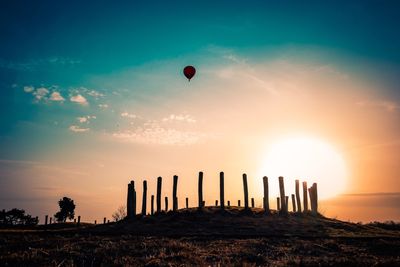 Silhouette people balloons on field against sky during sunset