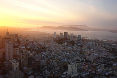 Aerial view of cityscape by sea against cloudy sky during sunset