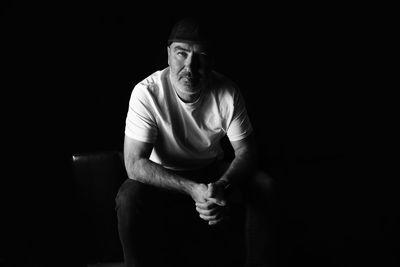 Portrait of young man sitting against black background